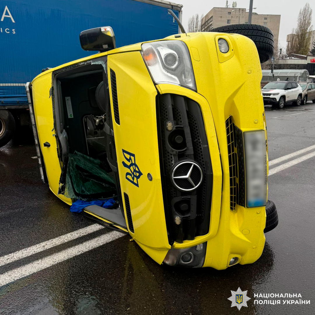 Перекинутий жовтий авто, мокра дорога, відкриті двері, наслідки зіткнення, що могло мати серйозні наслідки.