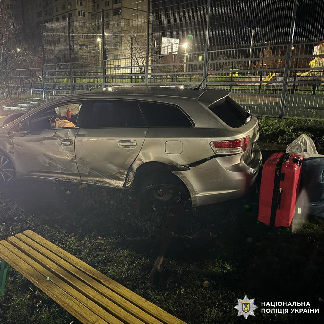 Передня частина авто сильно пошкоджена: капот зім’ятий, бампер і двигун деформовані. Навколо уламки автомобіля та конструкції. Подія сталася вночі, ймовірно, в парку або житловому районі.