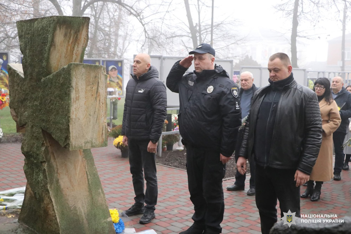 Поліцейські вшановують Героїв Небесної Сотні, військовослужбовців та всіх українців, які віддали життя за незалежність і свободу держави. Портрети з квітами нагадують про втрати. Туман і дерева створюють атмосферу скорботи.