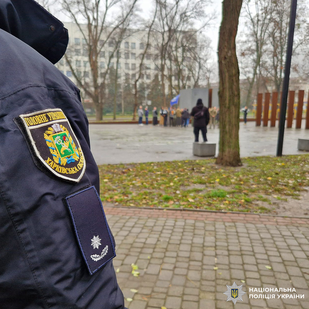 У парку зібралися люди для вшанування пам’яті. На тлі люди біля меморіалу, осінь, волога земля, тиша.