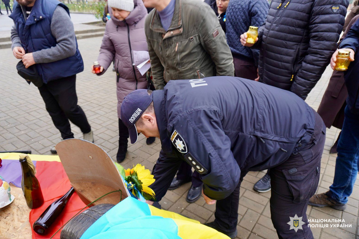 Поліцейські вшановують Героїв Небесної Сотні, військовослужбовців та всіх українців, які віддали життя за незалежність і свободу держави. Портрети з квітами нагадують про втрати. Туман і дерева створюють атмосферу скорботи.