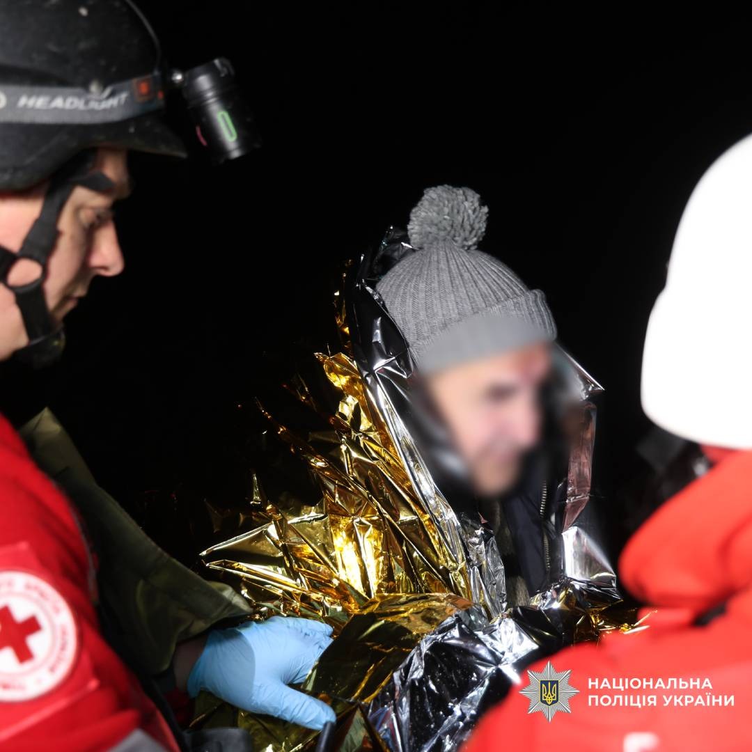 Рятувальники надають допомогу постраждалому, загорнутому в термоковдру. Видно медичні рукавички, шолом із ліхтарем.