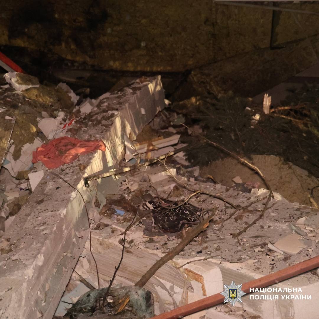 Бетонні плити, скручені металеві прути, уламки будівельних матеріалів і гілка дерева серед завалів. Нічна зйомка місця руйнування.