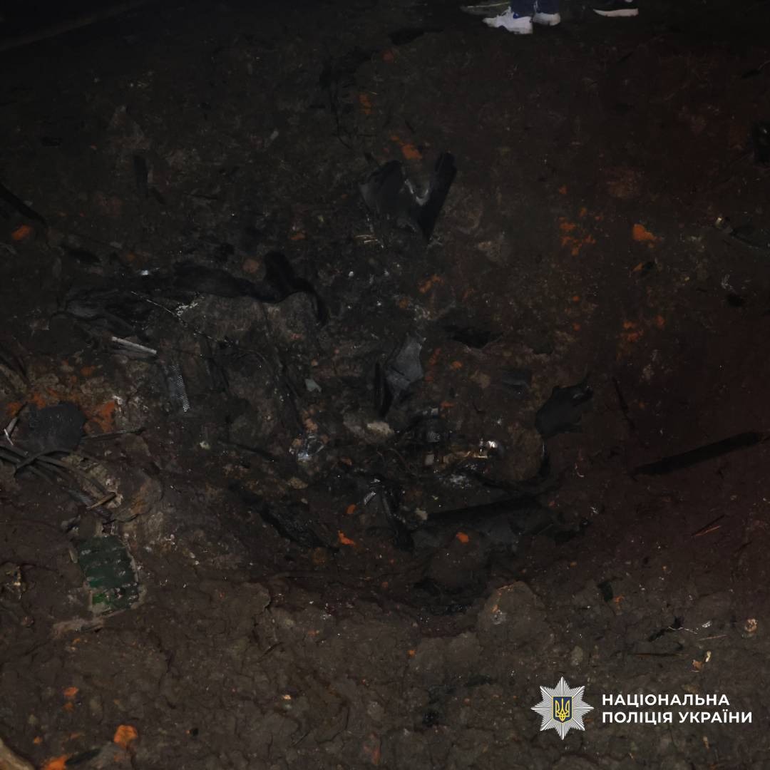 Нічне фото великої вирви в землі, ймовірно після вибуху. Навколо уламки металу та порушений ґрунт.