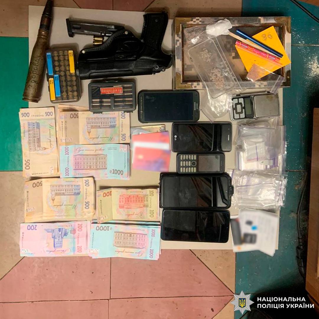 Вилучені речові докази: на підлозі розкладено зброю, боєприпаси, мобільні телефони, ваги, пакети з порошкоподібною речовиною, грошові кошти та інші предмети.