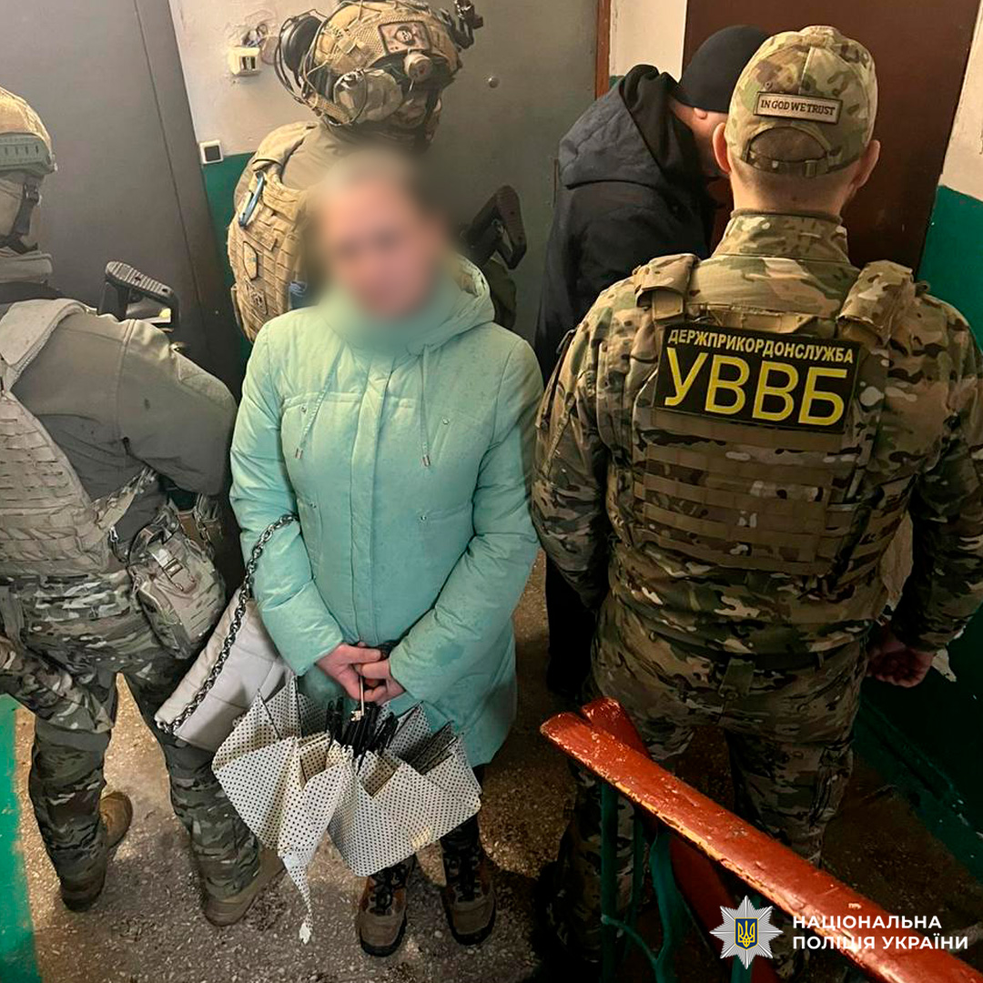 Співробітники Держприкордонслужби та Національної поліції України проводять слідчі дії в приміщенні. У центрі жінка одягнена в блакитне пальто, з парасолькою в руках. Правоохоронці екіпіровані в камуфляжну форму з тактичним спорядженням.