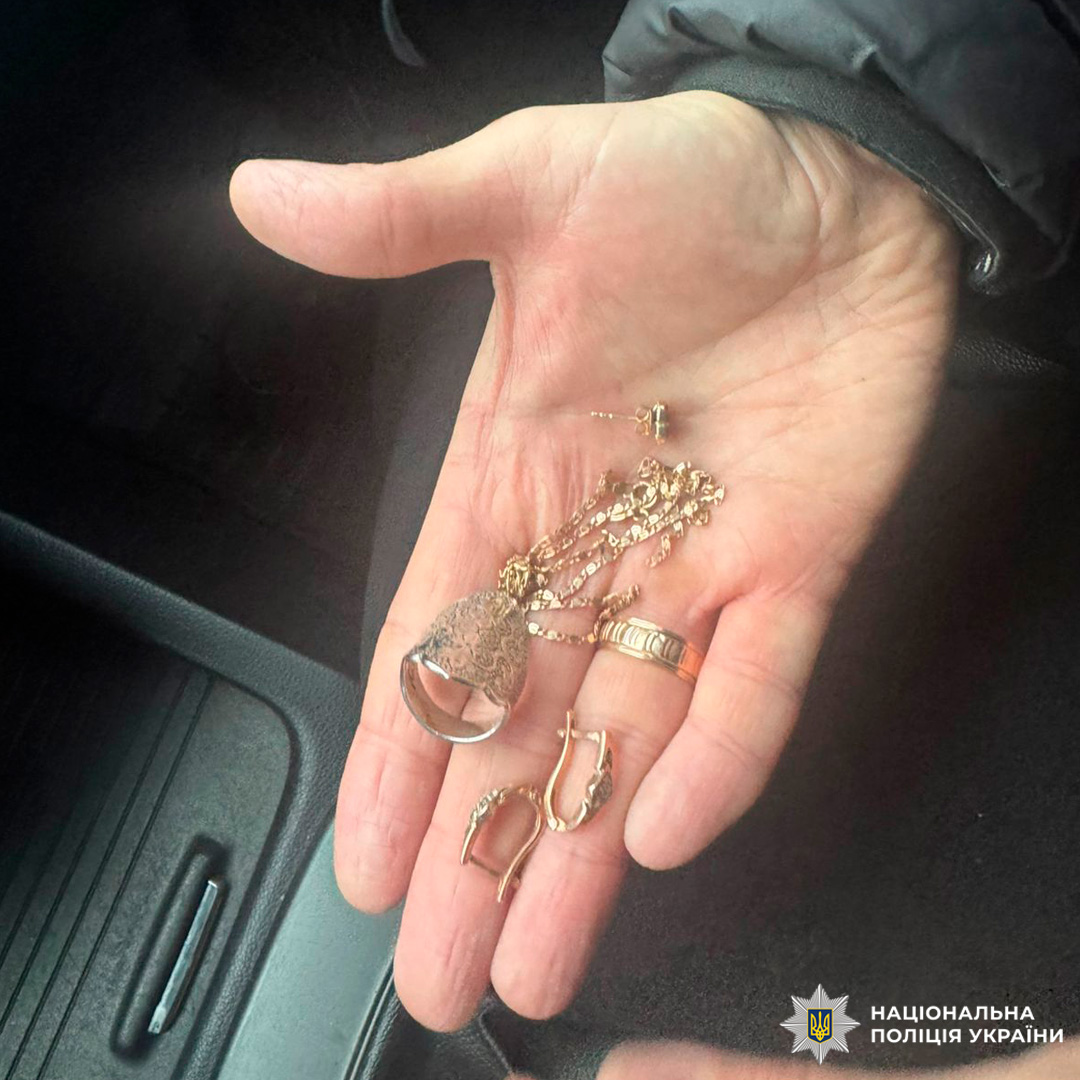 Під час слідчих дій зафіксовано вилучення ювелірних виробів: особа в темному одязі тримає в руці каблучку, ланцюжок із підвіскою та елементи сережок.