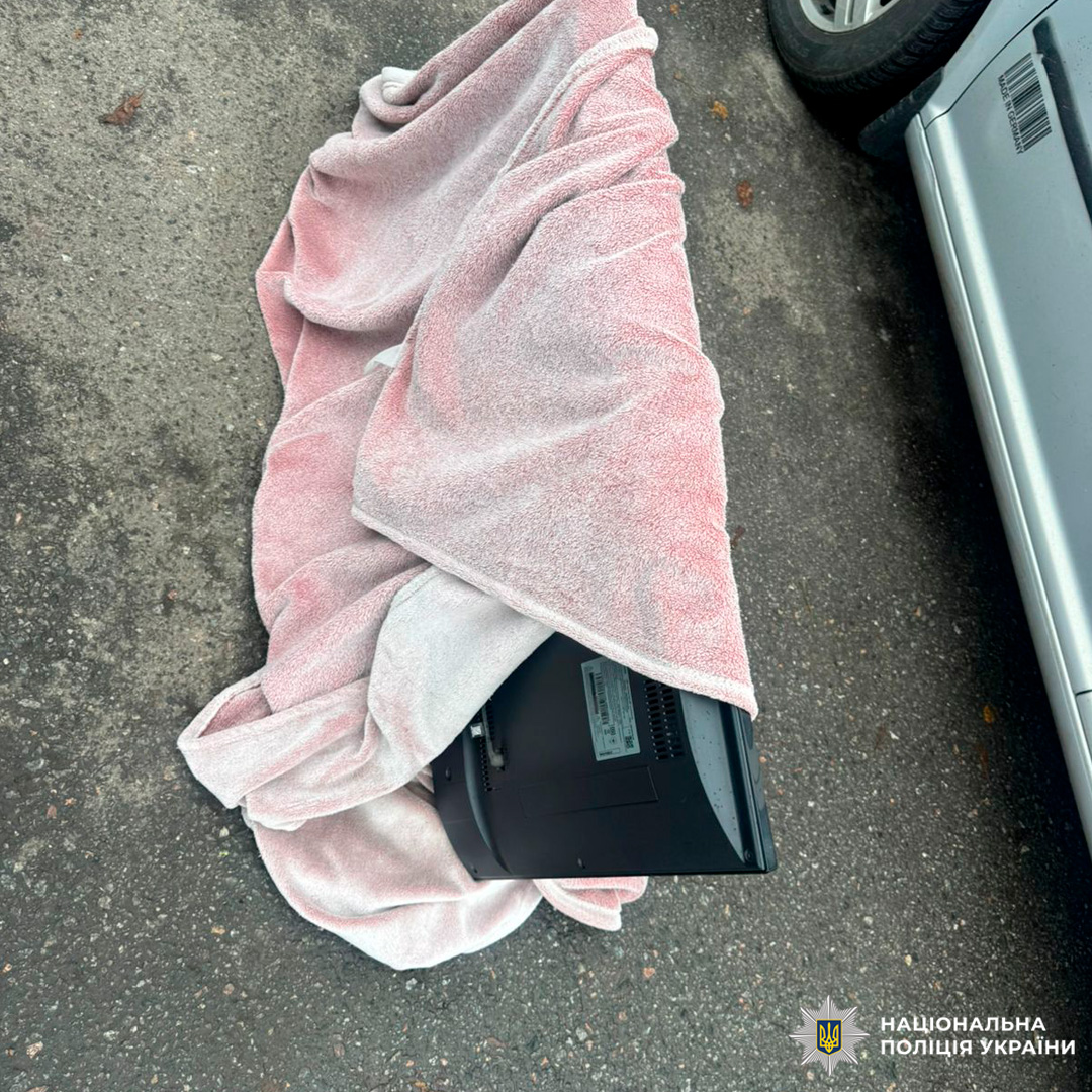 Під час слідчих дій зафіксовано комп’ютерний монітор, частково загорнутий у рушник, розміщений на асфальті поруч із сріблястим автомобілем.
