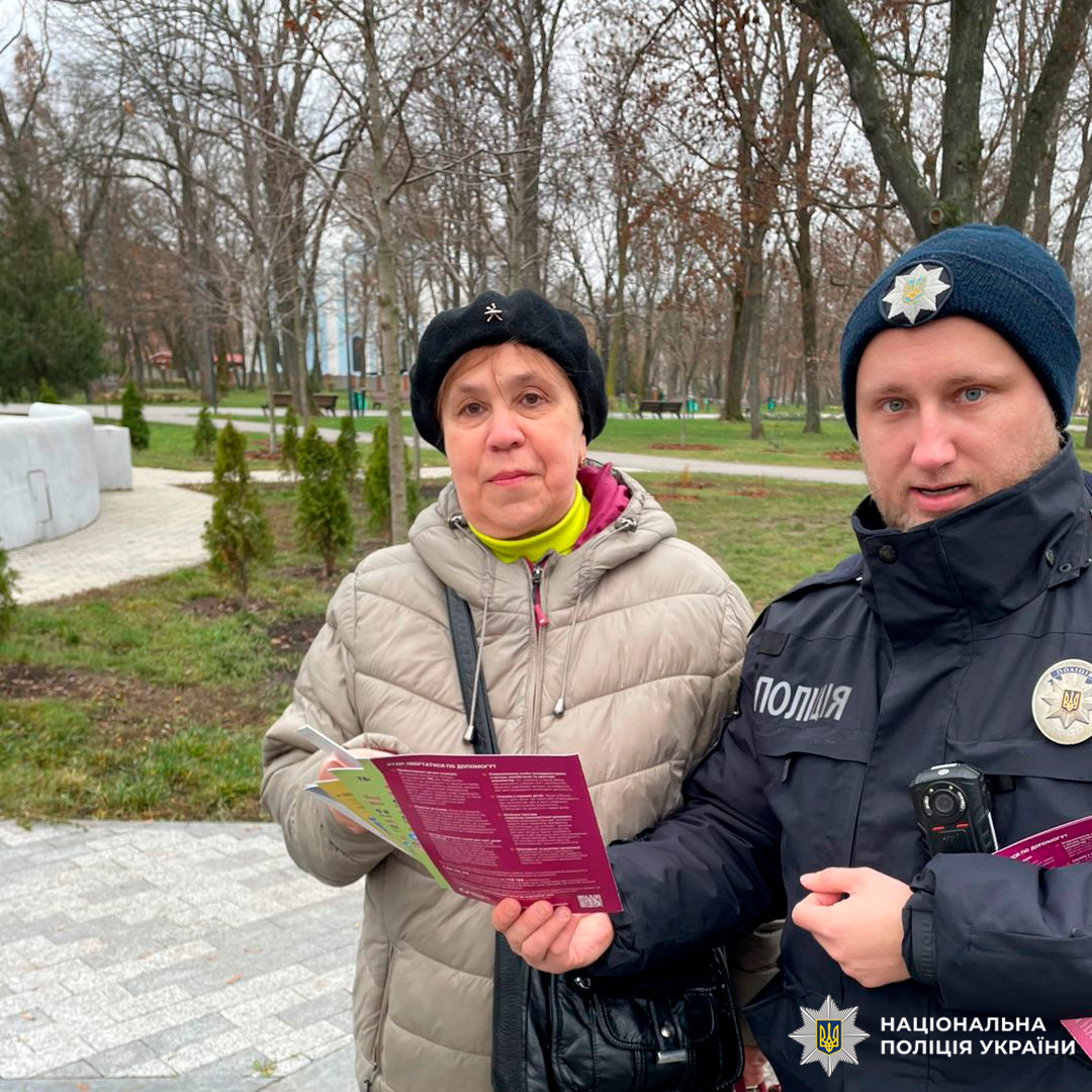 Поліцейський спілкується з літньою жінкою в парку, поширюючи інформаційні матеріали.