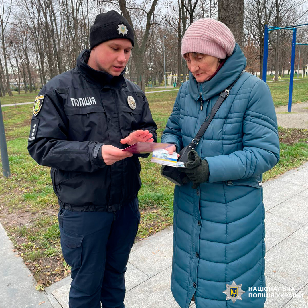 Поліцейський спілкується з літньою жінкою в парку, поширюючи інформаційні матеріали.