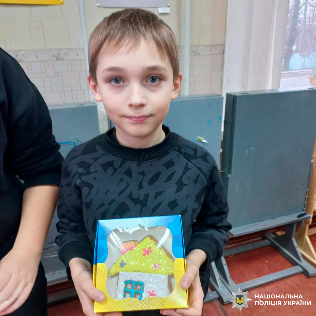 Дитина тримає пряник, прикрашений кольоровою глазур’ю, у коробці з синьо-жовтим оформленням.