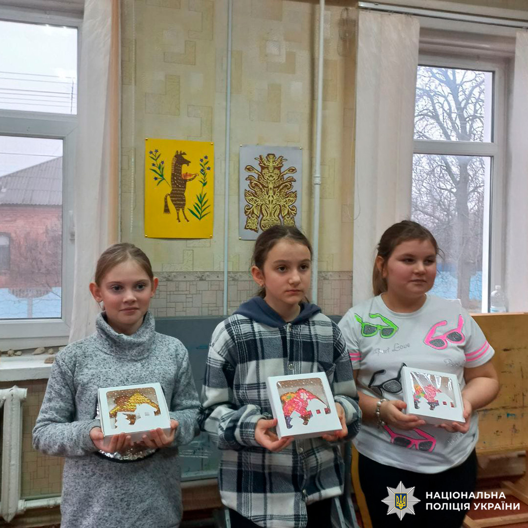 У класному приміщенні троє дітей тримають оформлені художні роботи з зображенням.