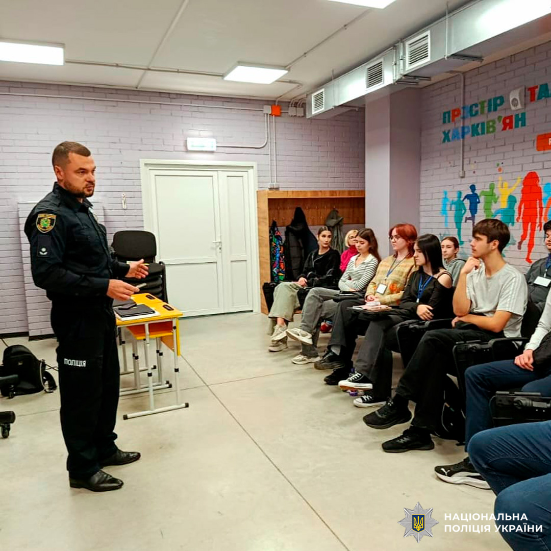 Співробітник Національної поліції України проводить лекцію для групи молодих людей. Учасники уважно слухають, деякі роблять нотатки.