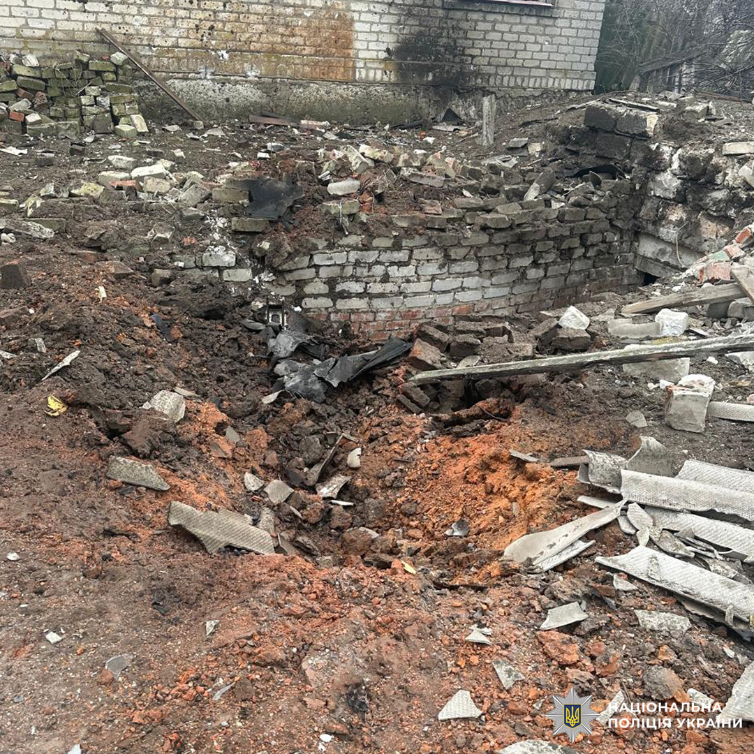 Пошкоджена ділянка перед будівлею з вирвою та розкиданими уламками.