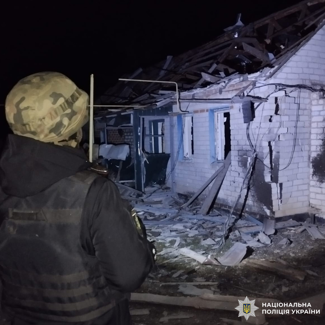 Поліцейський на тлі пошкодженої будівлі вночі.