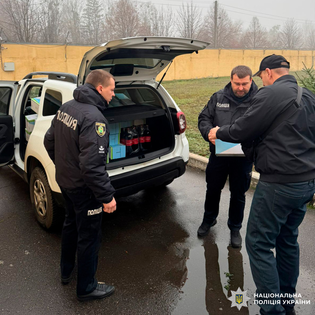 Троє поліцейських біля відкритого багажника службового авто, заповненого коробками та пляшками. Один тримає коробку.