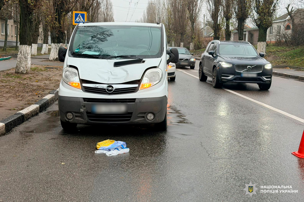 Білий мікроавтобус із пошкодженим капотом і лобовим склом зупинений на мокрій дорозі біля пішохідного переходу. На асфальті розкидані речі та дорожній конус.