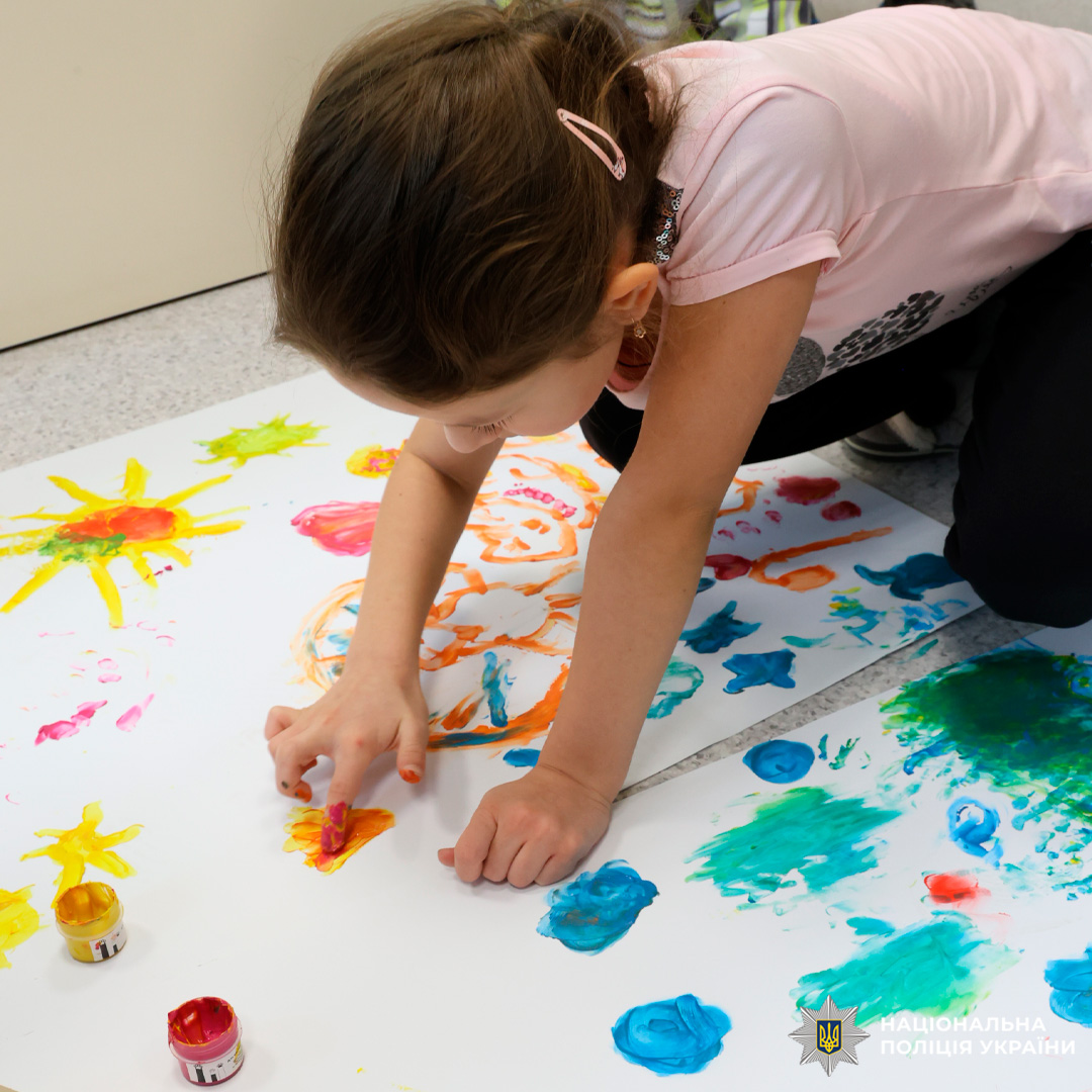 Дитина малює пальчиковими фарбами на великому аркуші паперу.