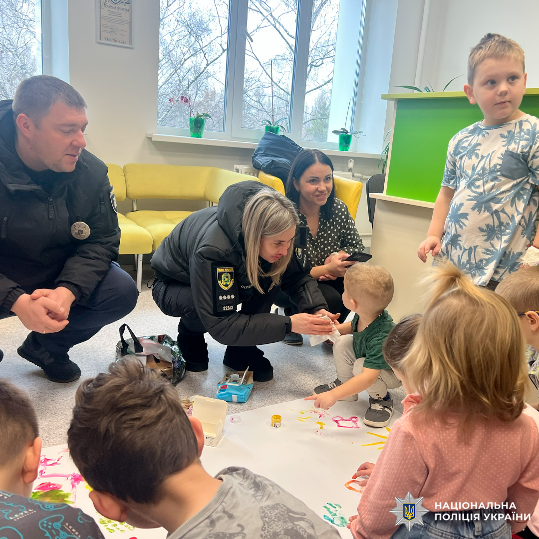 Діти малюють на великому аркуші паперу в присутності дорослих, серед яких працівники поліції.