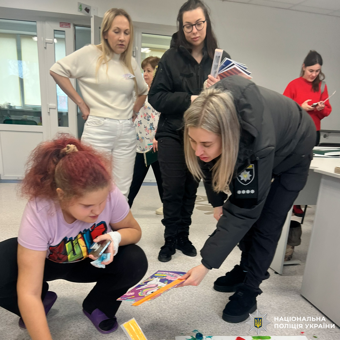 Діти малюють на великому аркуші паперу в присутності дорослих, серед яких працівники поліції.
