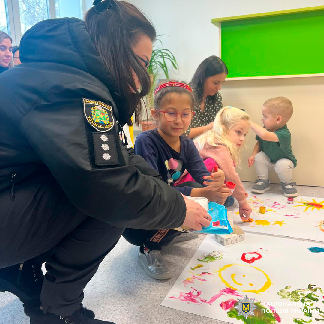 Діти малюють на великому аркуші паперу в присутності дорослих, серед яких працівники поліції.