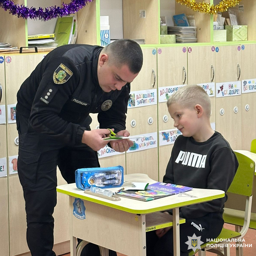 Поліцейський допомагає дитині з творчим завданням у класі.