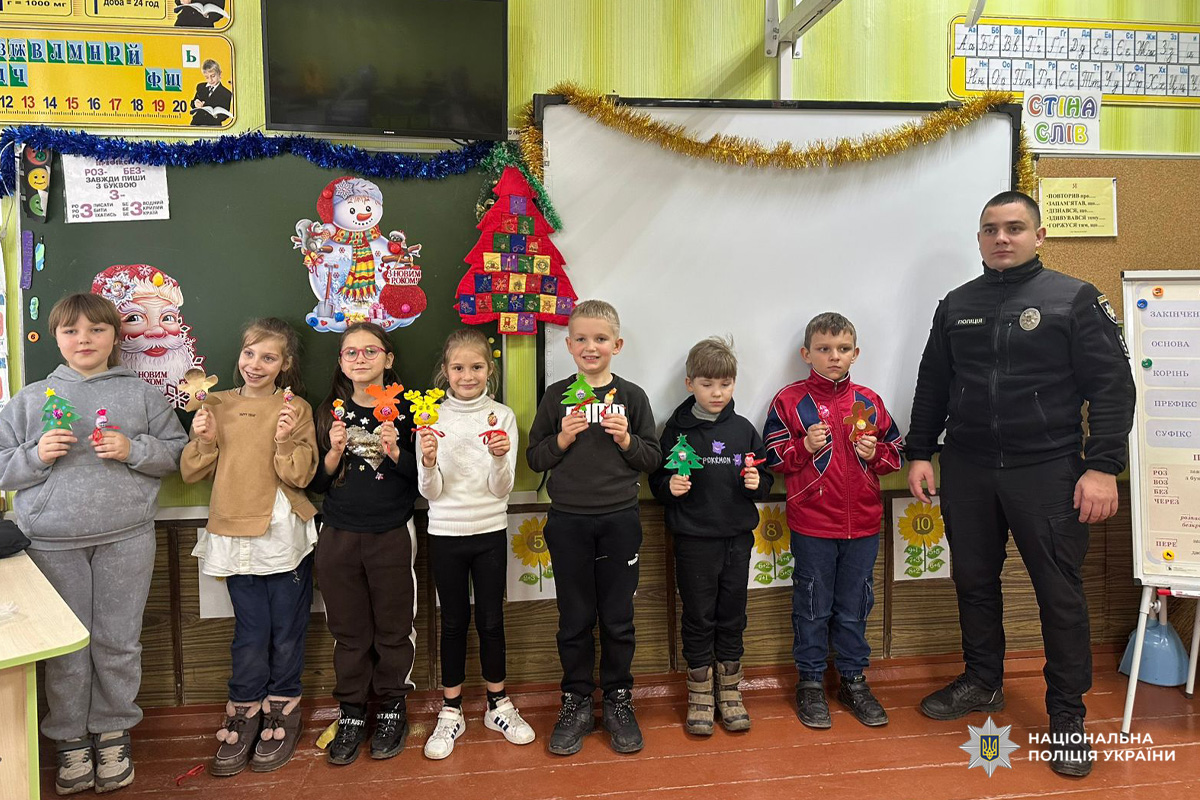 Поліцейський разом із дітьми в класі під час святкового заходу. Кожна дитина тримає новорічну прикрасу.