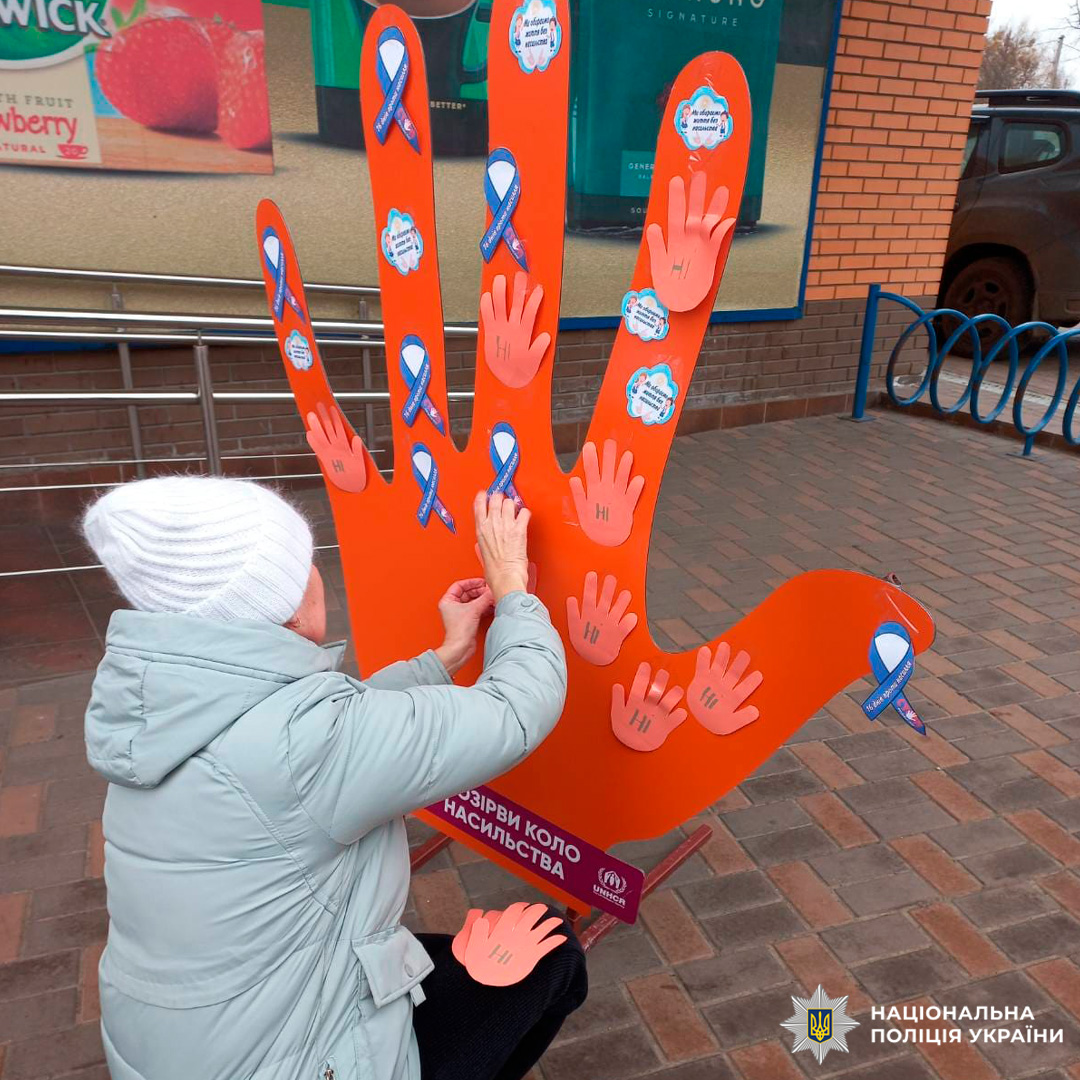 Учасниця соціальної акції прикріплює символічну долоньку до інсталяції «Розірви коло насильства» біля торгового закладу.