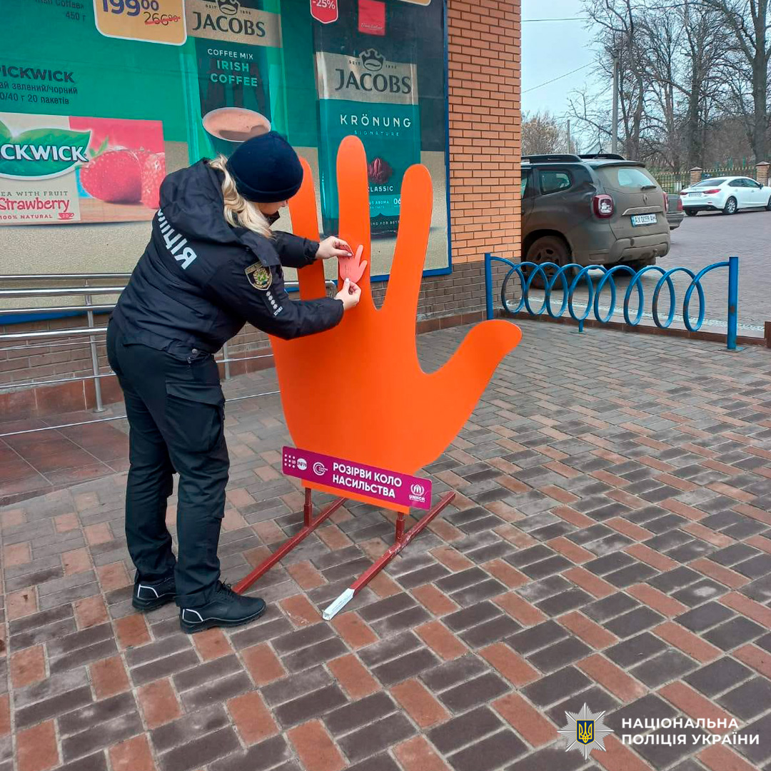 Співробітник поліції прикріплює символічну долоньку до інсталяції «Розірви коло насильства» біля торгового закладу.