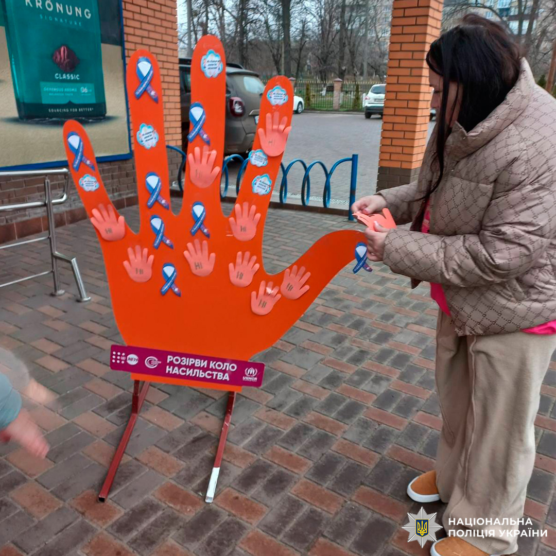 Учасниця соціальної акції прикріплює символічну долоньку до інсталяції «Розірви коло насильства» біля торгового закладу.