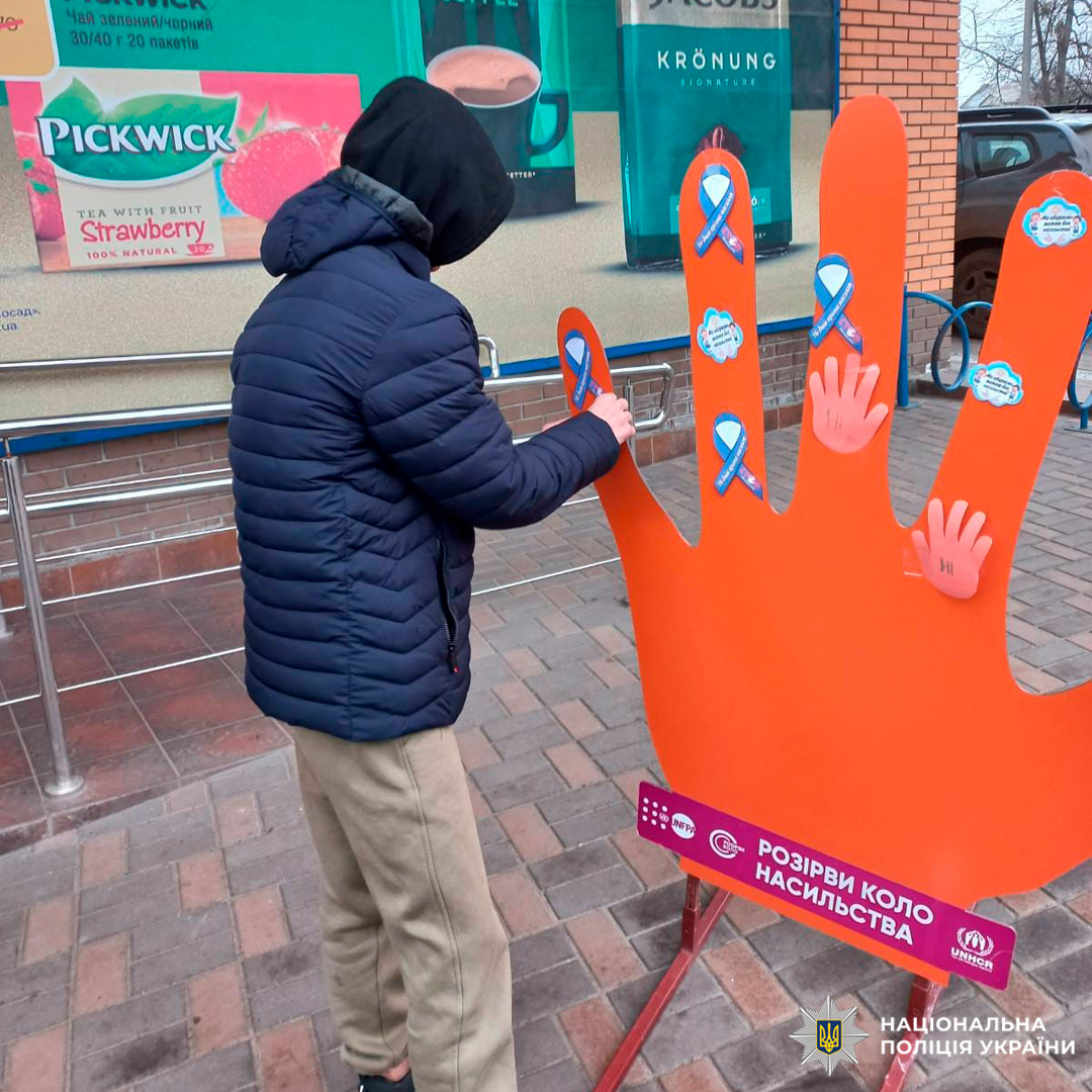 Учасниця соціальної акції прикріплює символічну долоньку до інсталяції «Розірви коло насильства» біля торгового закладу.