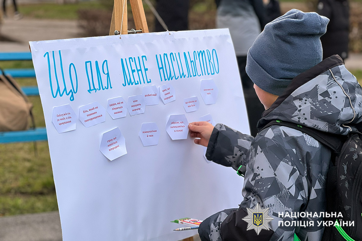 Хлопчик наклеює відповідь на стенд "Що для мене насильство?"