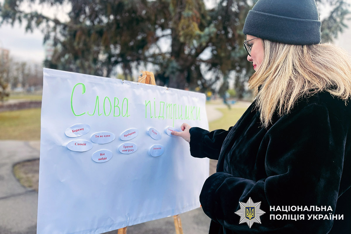 Жінка наклеює відповідь на стенд "Що для мене насильство?"