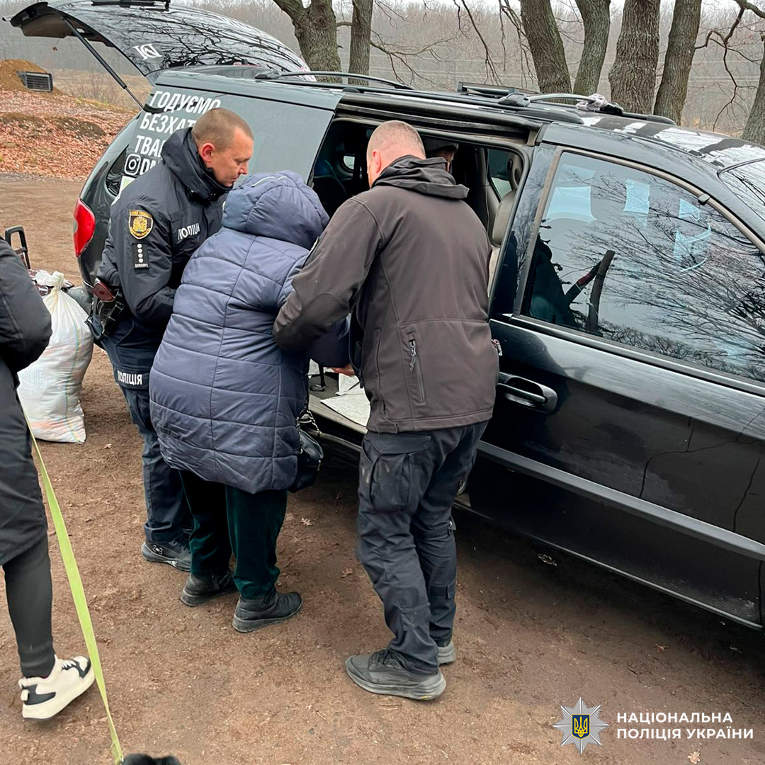 Поліцейські допомагають людині сісти до службового авто в лісистій місцевості.