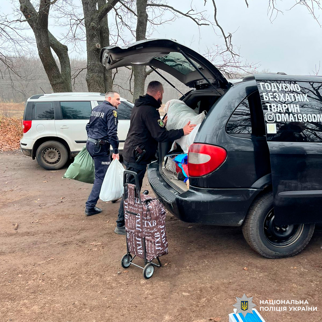 Поліцейські завантажують великі пакети до службового авто в лісистій місцевості.