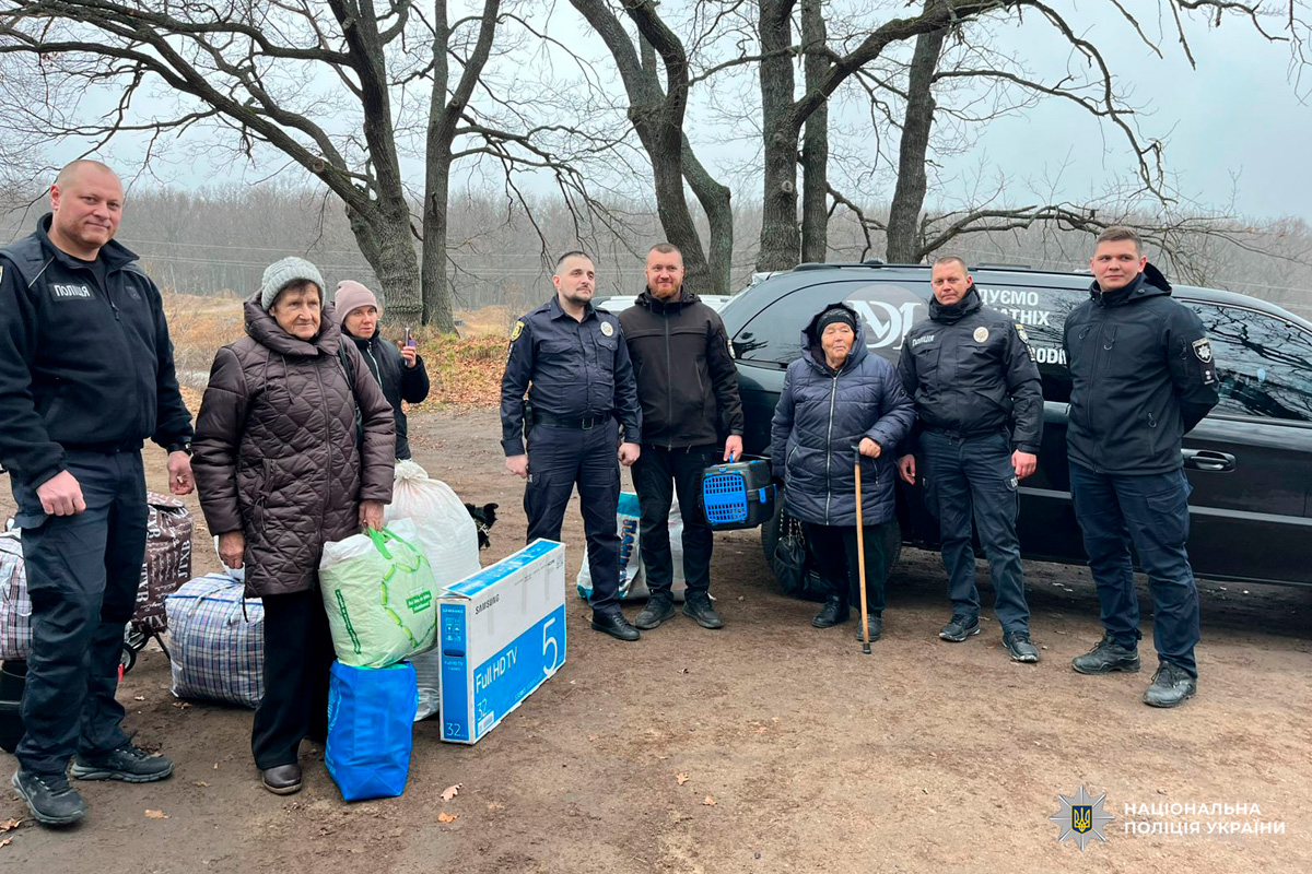 Працівники поліції та літні цивільні, у лісистій місцевості. Поруч речі для транспортування, зокрема коробка з телевізором, сумки, переноска для тварин і тростина. На задньому плані службовий автомобіль.