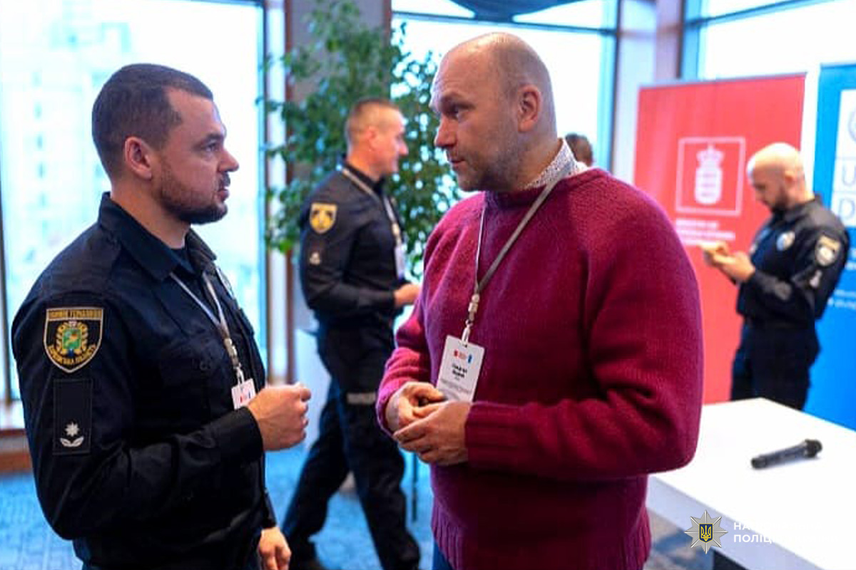 Представники поліції та учасники конференції спілкуються на тлі банерів.