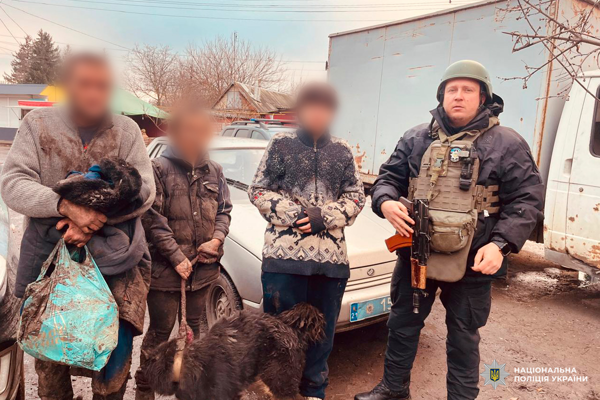 Поліцейський у бронежилеті та шоломі стоїть поруч із трьома цивільними.