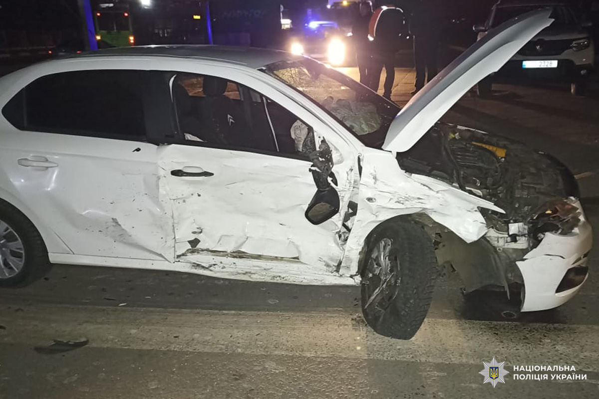 Легковий автомобіль із деформованою передньою частиною після ДТП, на тлі працюють екстрені служби.