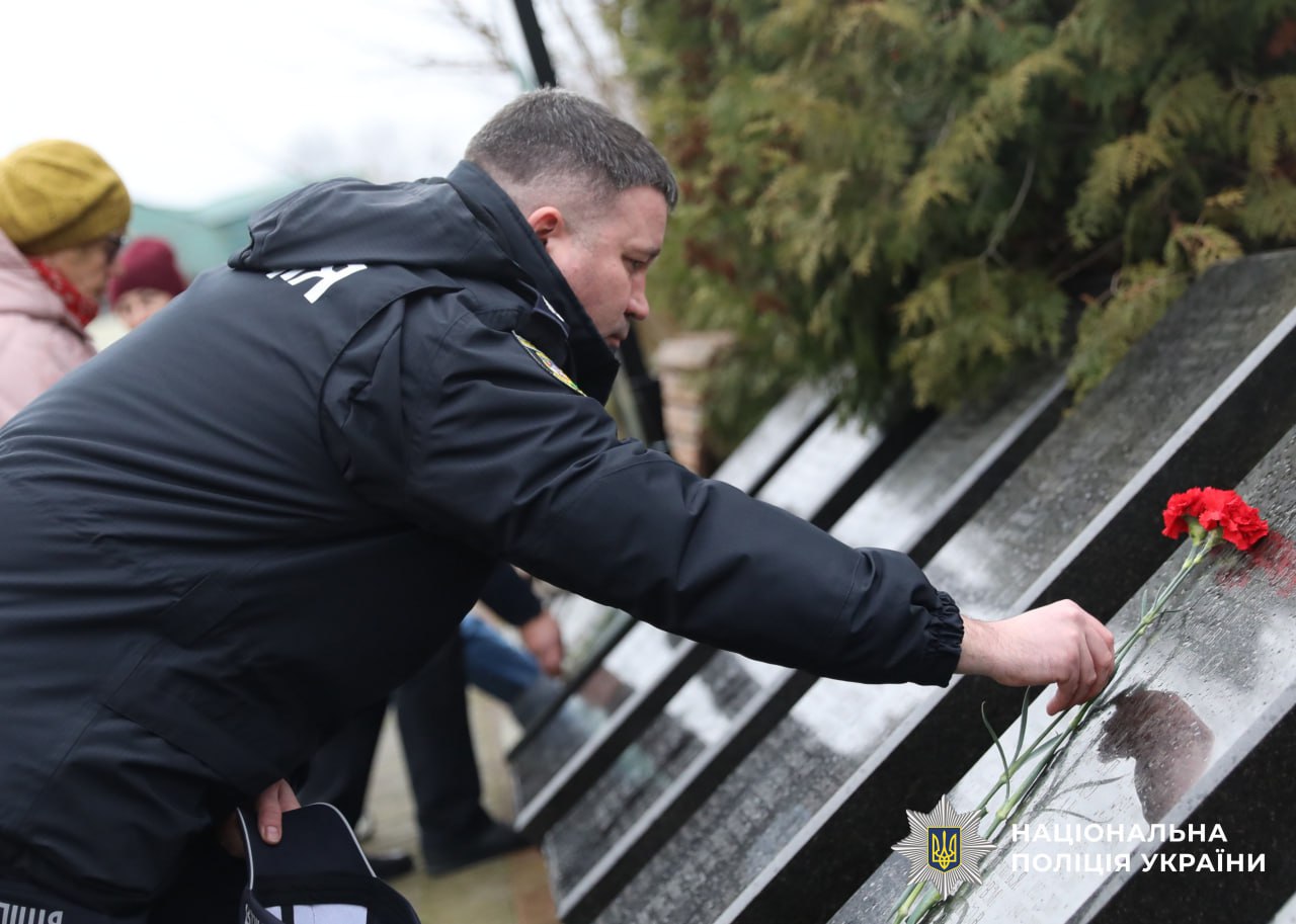 На фото поліцейський кладе квіти до мемореалу.