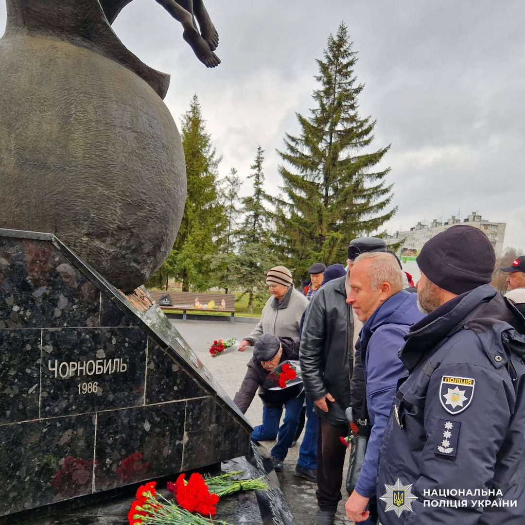 Поліцейський та громадяни покладають квіти до меморіалу.