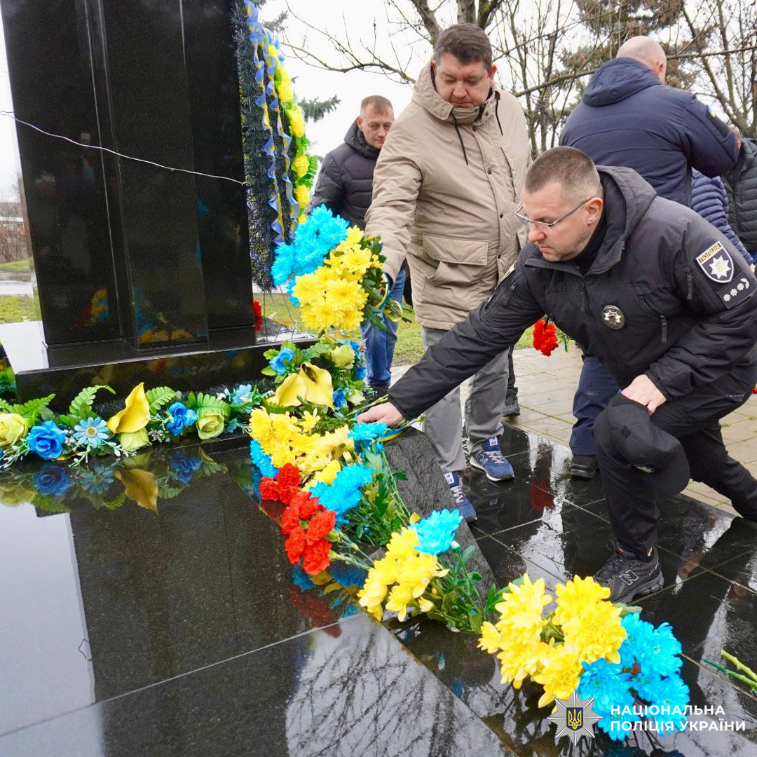 Поліцейський та громадяни покладають квіти до меморіалу.