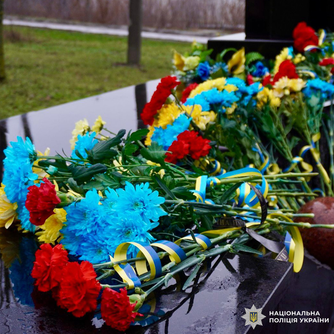 Квіти з синьо‑жовтими стрічками покладені на чорну кам’яну плиту.