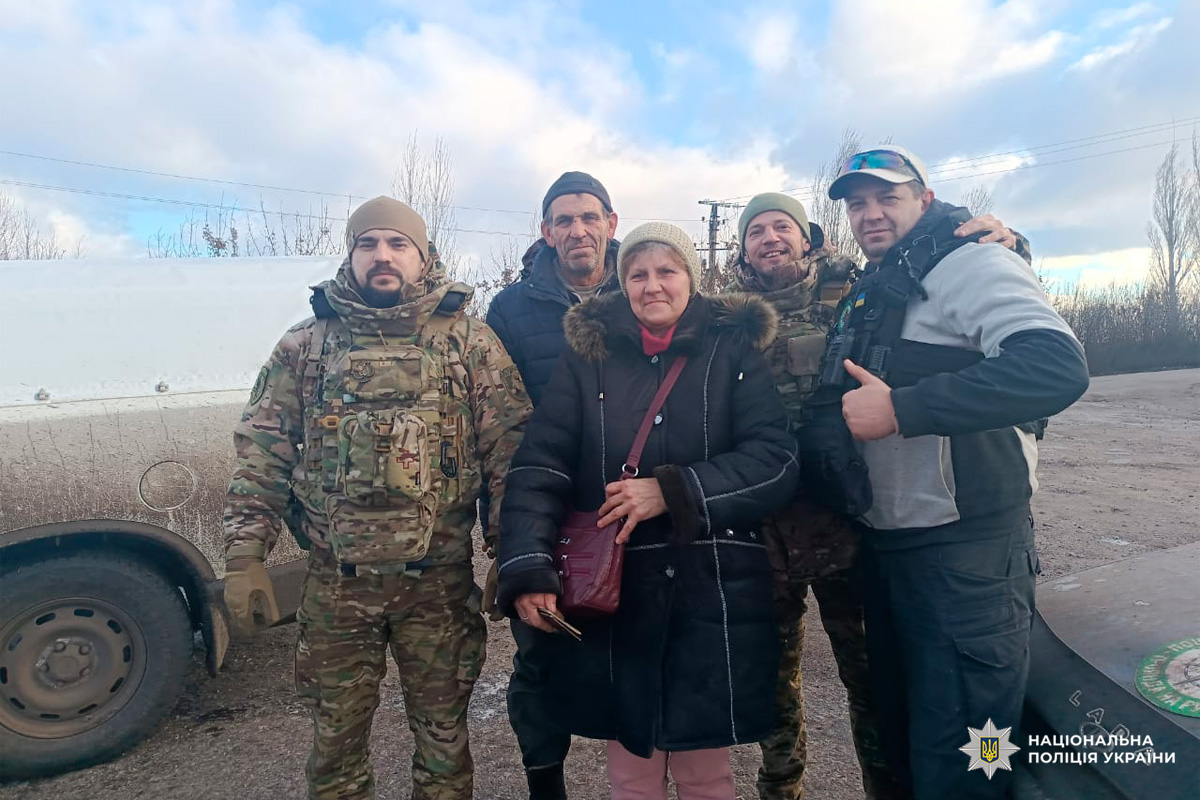 Правоохоронці та цивільна жінка біля автомобіля на тлі зимового пейзажу.