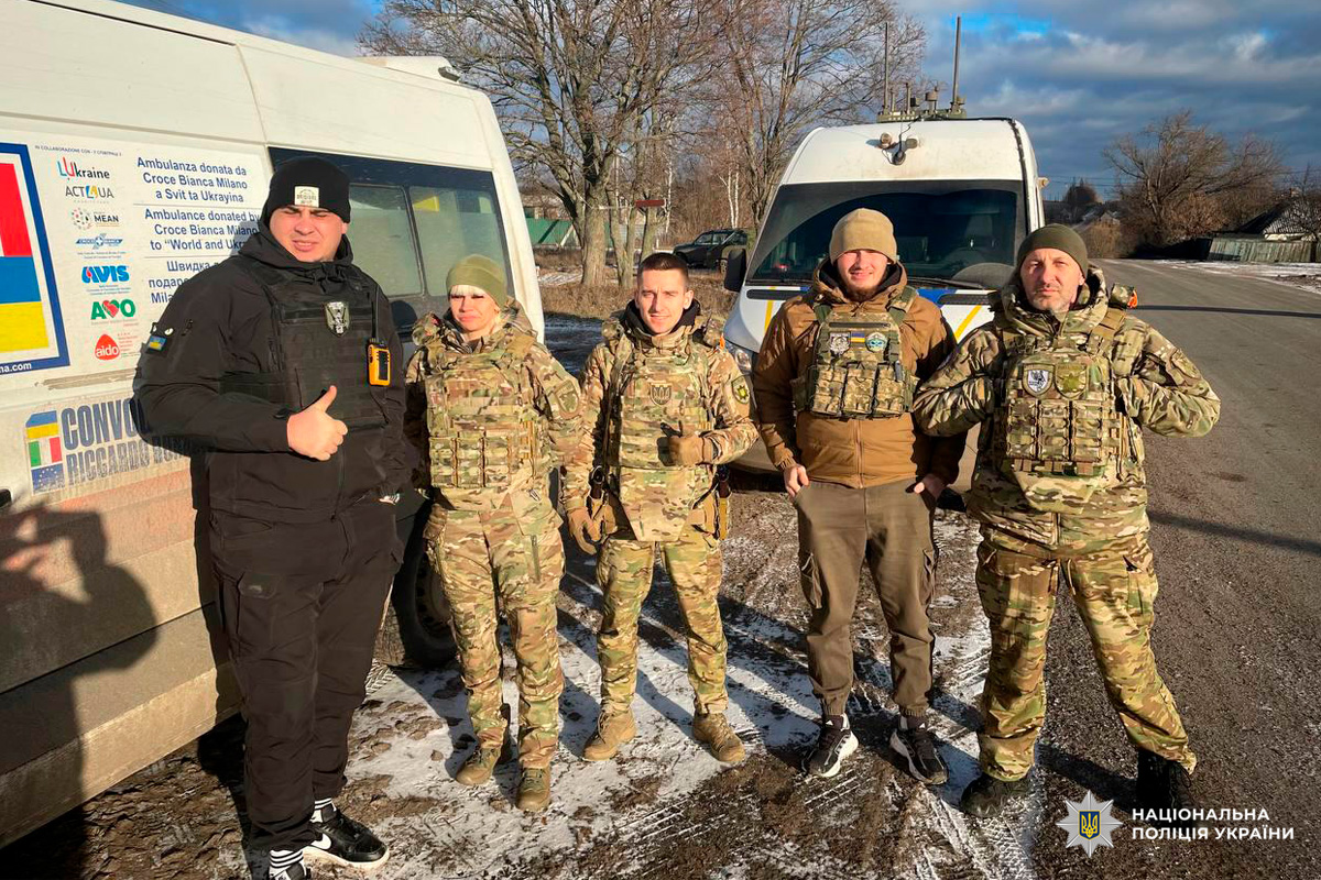 Співробітники поліції в тактичному спорядженні біля двох автомобілів, включно з каретою швидкої допомоги.