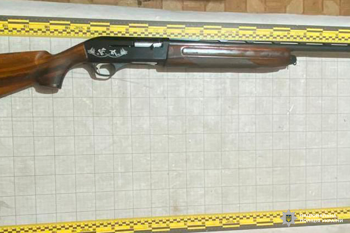 Гладкоствольна рушниця з дерев’яним прикладом і різьбленим металевим коробом, розміщена на фоні з вимірювальною сіткою та жовто‑чорною масштабною шкалою.