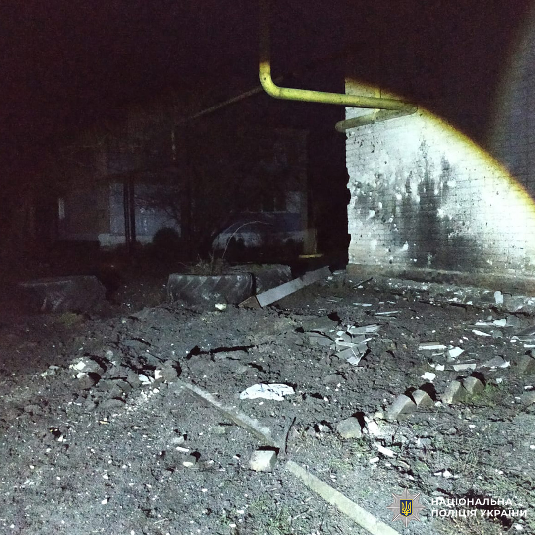 Уламки та сміття розкидані біля стіни будівлі з ознаками пошкоджень, фото зроблено вночі.