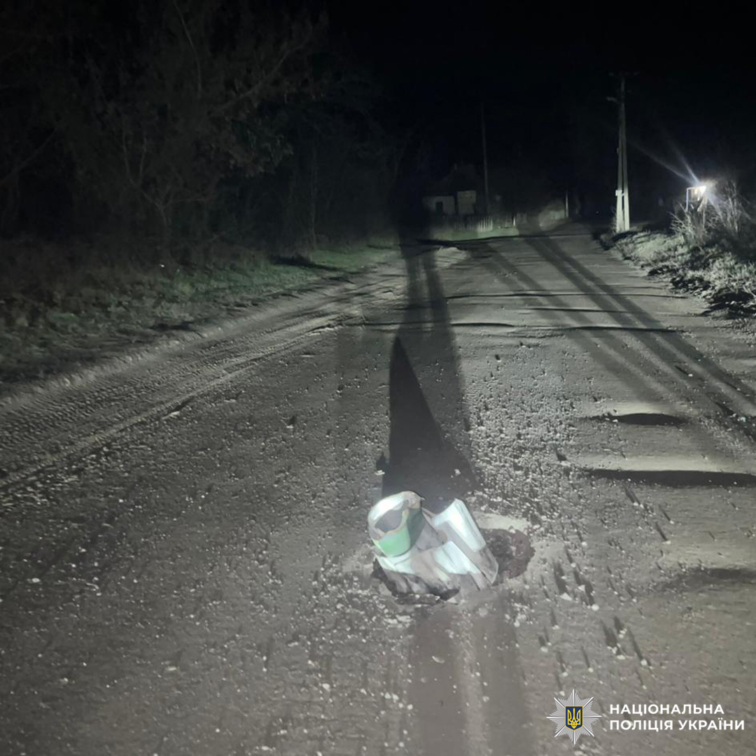 Великий металевий предмет знаходиться на нічній дорозі, навколо видно сліди пошкодження та тінь від фар.