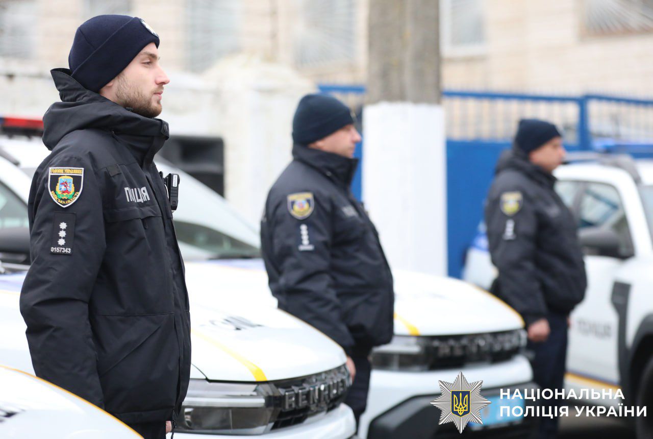 На фото зображені працівники поліції біля службових авто