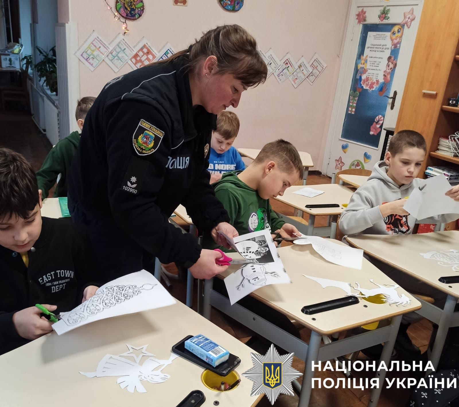 На фото поліцейська та діти разом роблять поробки з паперу.